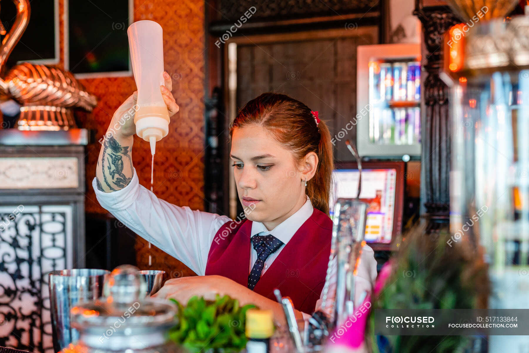 Serious female bartender in uniform standing at counter in bar and ...