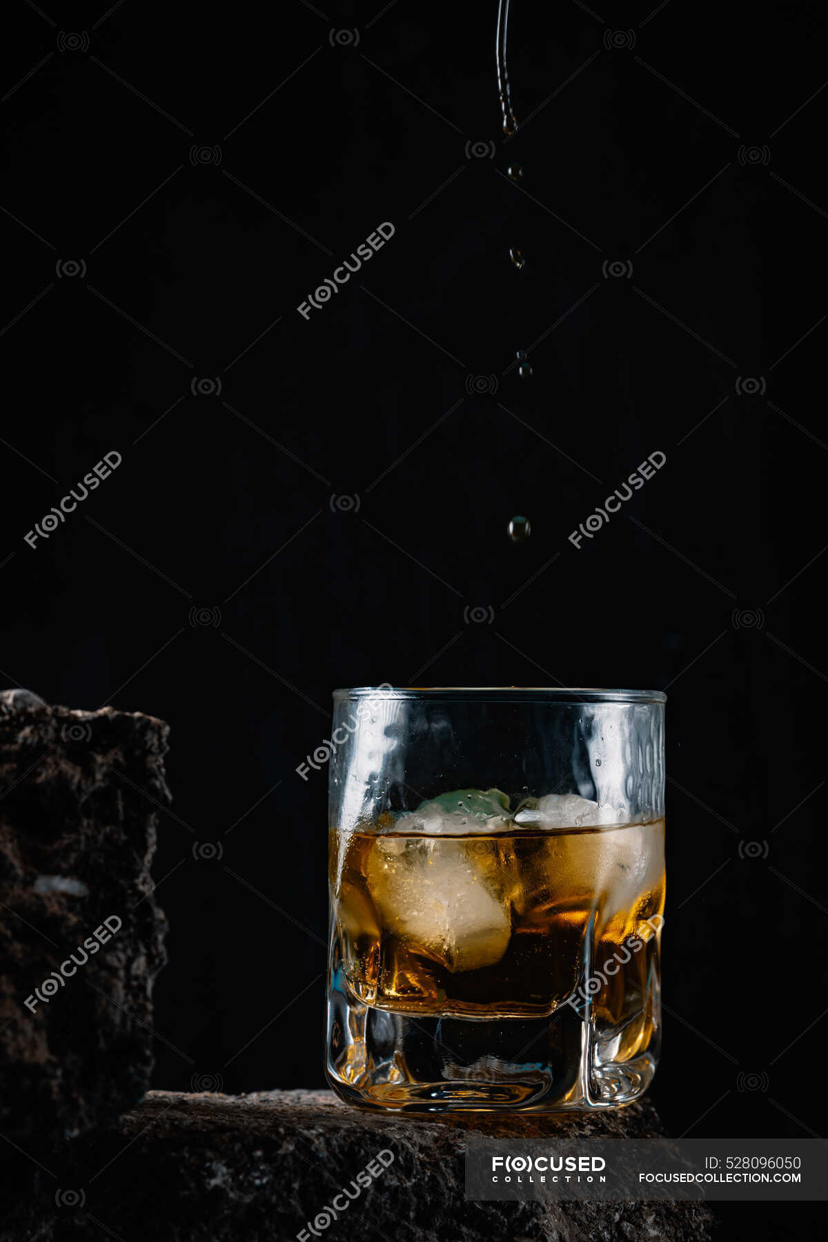 WhiskeyTropfen fallen auf Eiswürfel, die in Kristallglas auf rauer