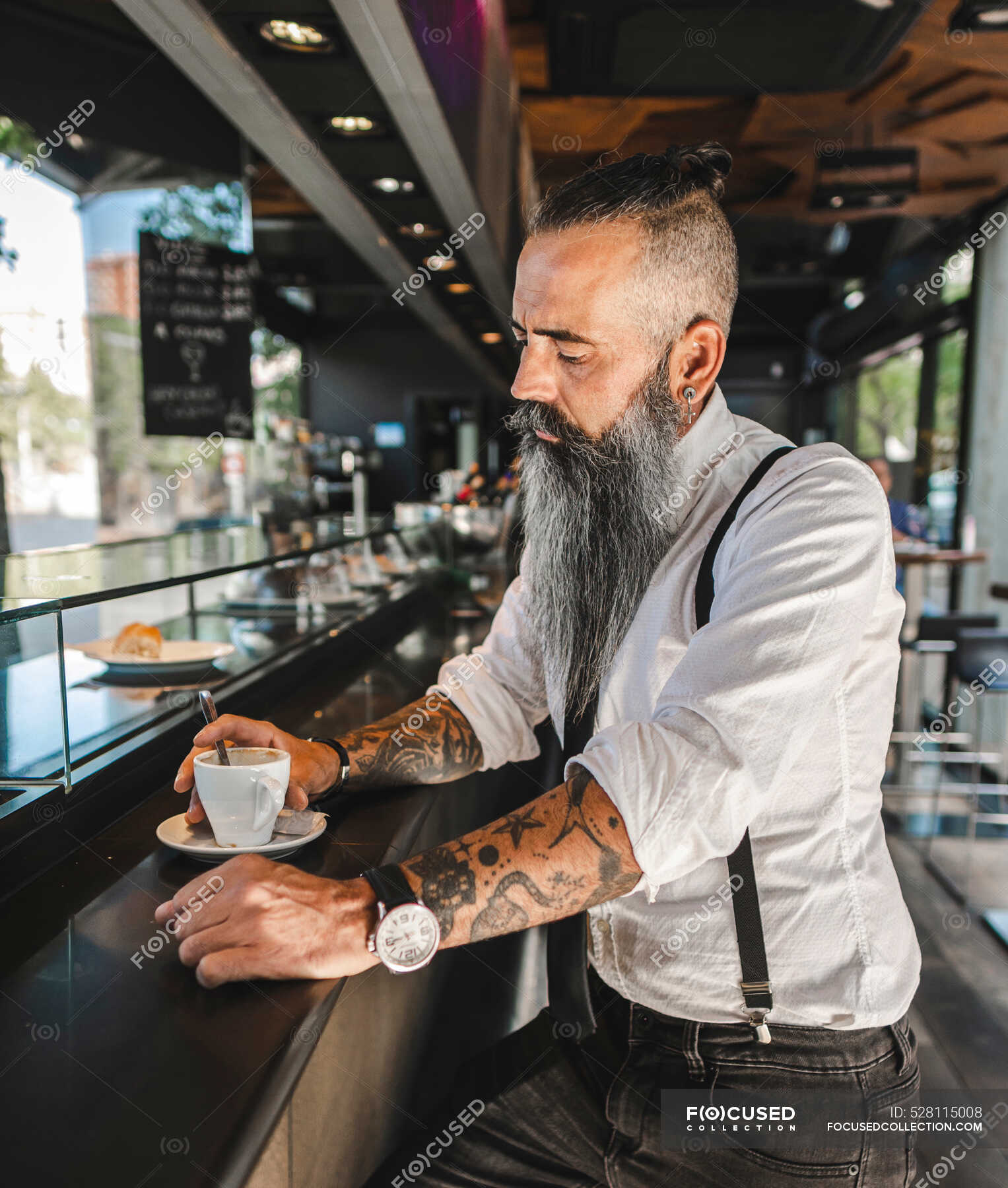 Side view of serious bearded businessman with tattoo in classy outfit  drinking coffee while sitting at counter in modern cafeteria — Hot Drink,  hipster - Stock Photo | #528115008