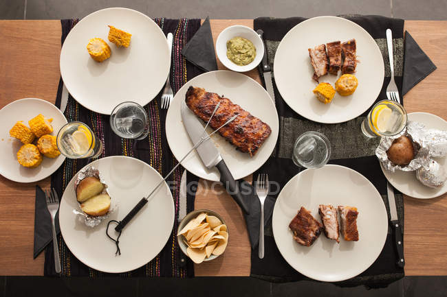 Tavolo con costolette alla griglia, patate e mais — Foto stock