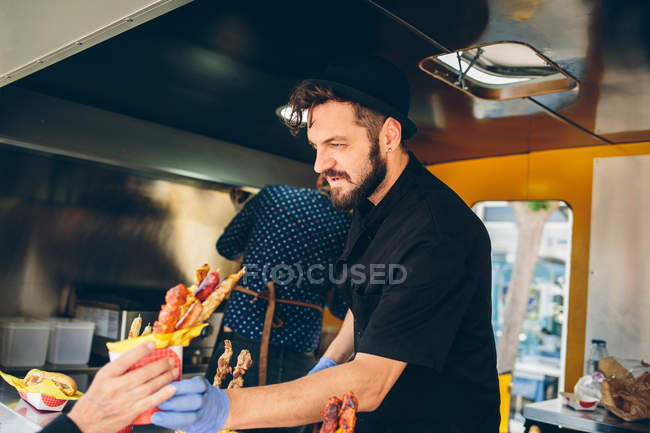Hipster em chapéu vendendo comida em caminhão de alimentos — Fotografia de Stock