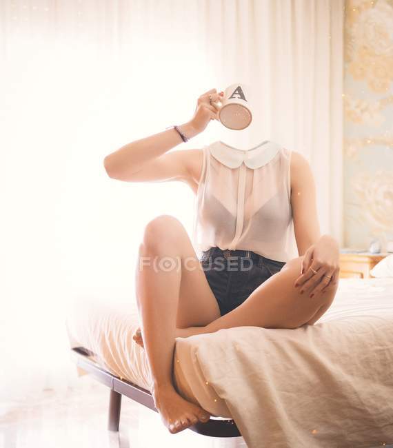 Donna senza testa che siede sul letto e beve — Foto stock
