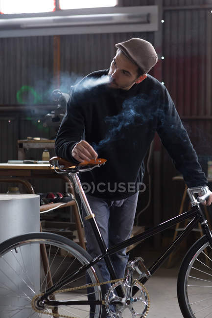 Ремесленник курит, держа в руках новый велосипед — стоковое фото