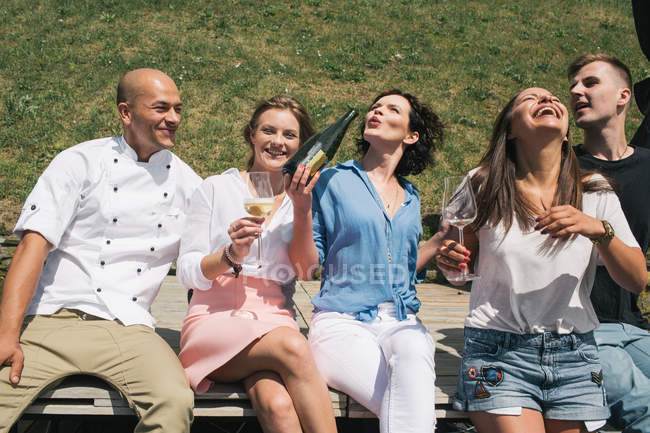 Друзья с шампанским сидят на открытом воздухе — стоковое фото
