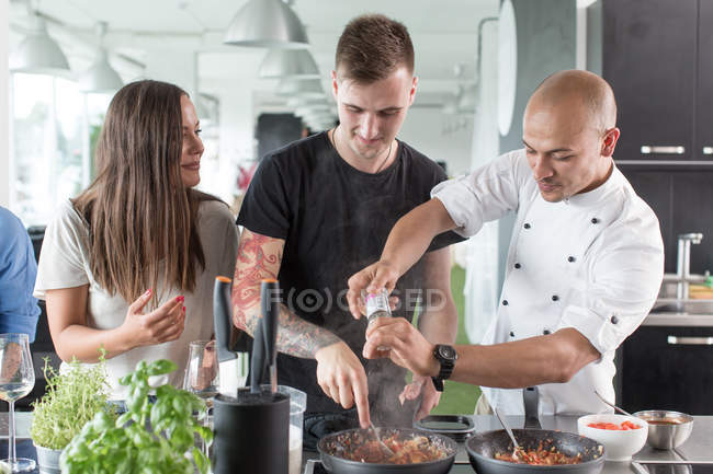 Chef salpimentando comida con estudiantes - foto de stock