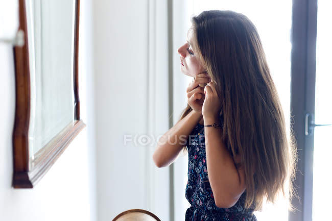 Mujer joven poniendo pendiente - foto de stock