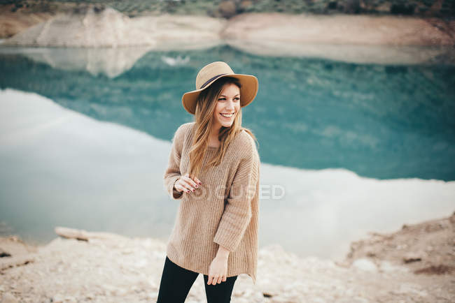 Веселая женщина в шляпе против озера — стоковое фото