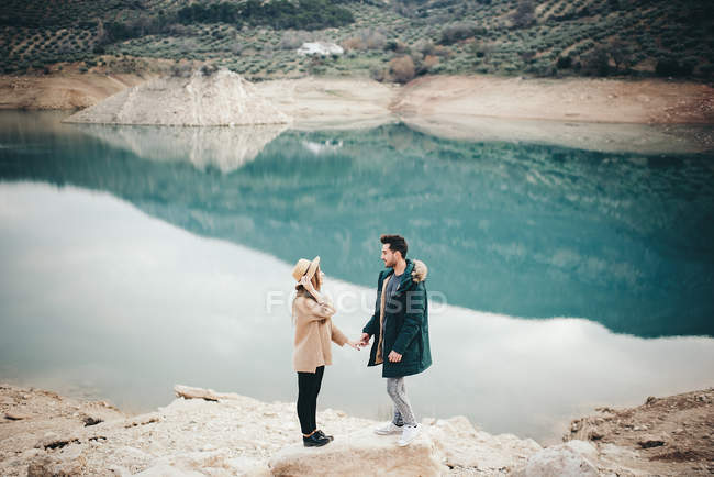Вид сбоку пары, держащейся за руки на берегу озера — стоковое фото