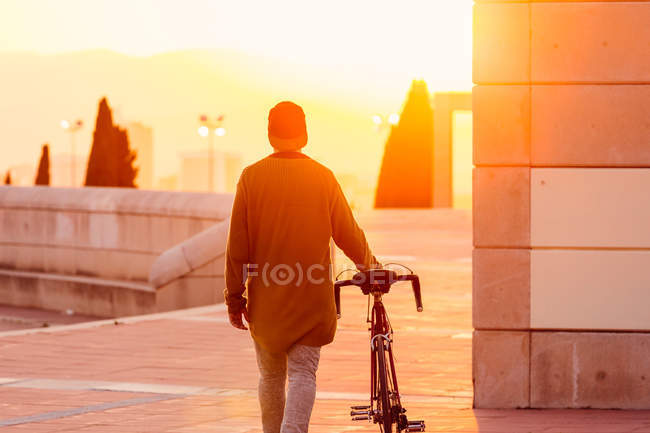 Uomo a piedi con la bicicletta mentre il tramonto — Foto stock