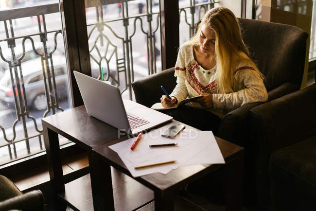 Mujer rubia escribiendo en planificador en la cafetería - foto de stock