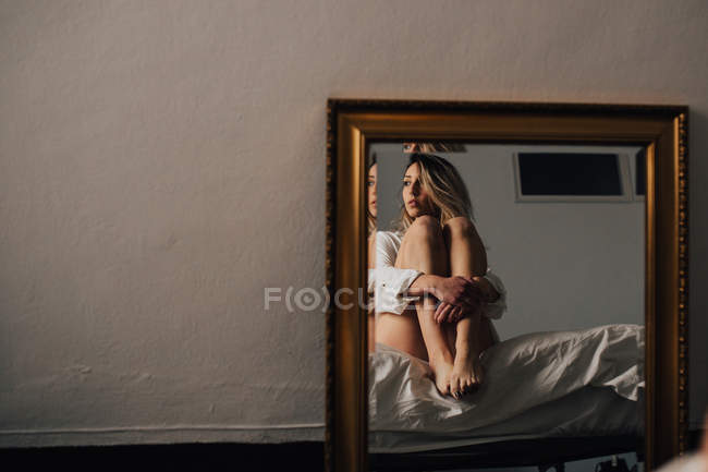 Reflection of female embracing her knees — Stock Photo