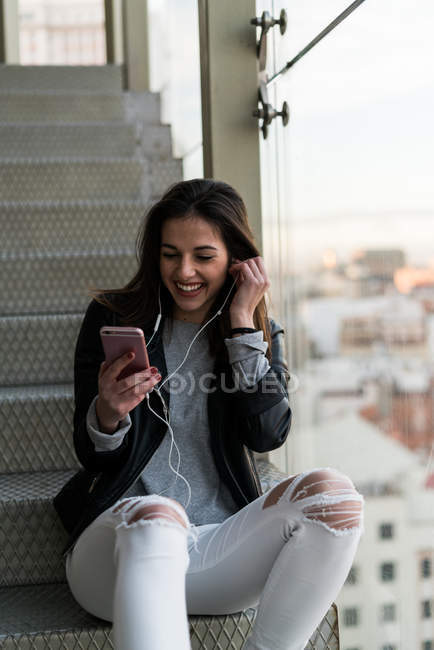 Young woman listening to music on stairs — Stock Photo