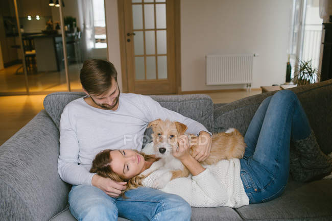 Пара гладить собаку на дивані — стокове фото