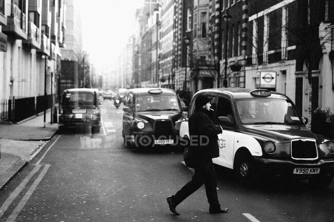 Vue sur la ville en noir et blanc de la circulation londonienne dans les rues. Homme fumeur traversant la rue contre les taxis. — Photo de stock