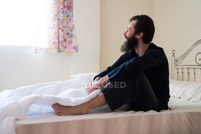 Uomo barbuto seduto a letto — Foto stock