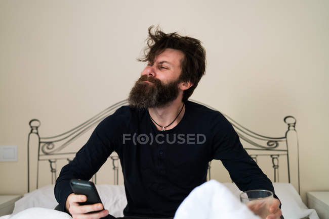 Schläfriger Mann mit Telefon im Bett — Stockfoto