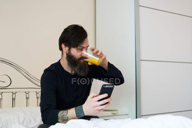Schläfriger Mann mit Telefon im Bett — Stockfoto
