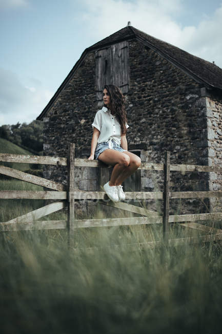 Женщина сидит на деревянном заборе — стоковое фото