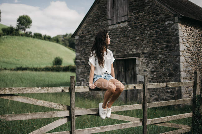 Женщина сидит на деревянном заборе — стоковое фото