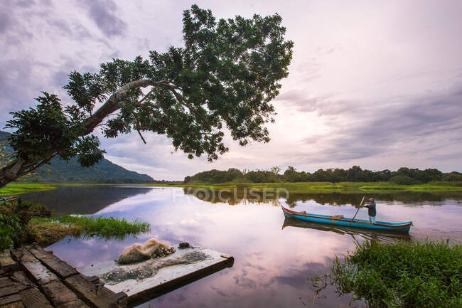 Pessoa anônima flutuando na canoa na água do rio com vista para a paisagem tropical. — Fotografia de Stock