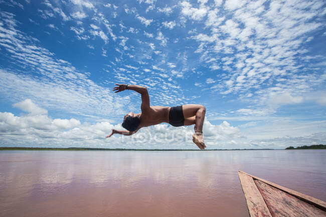 Вид збоку людини в русі стрибка з дзьоба човна в морі . — стокове фото