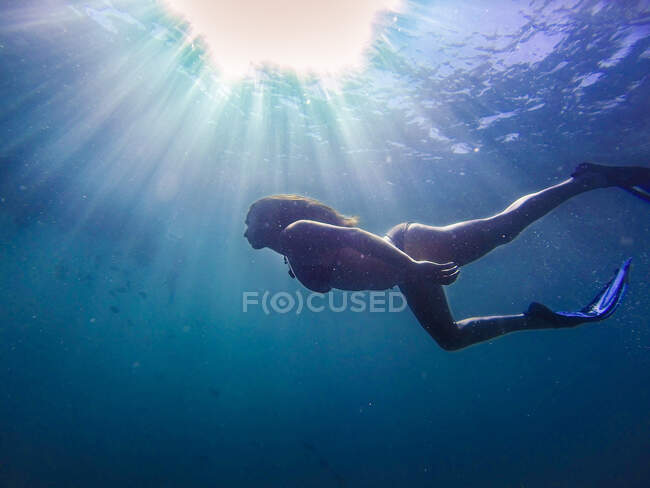 Side view of girl in swimsuit and flippers swimming in sunlight underwater. — Stock Photo