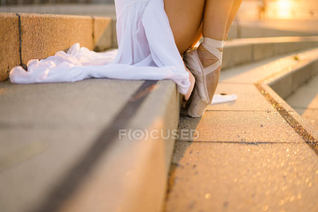 Low section of ballerina wearing point shoes and white dress standing on steps — Stock Photo