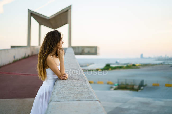 Brünettes Mädchen lehnt am steinernen Geländer und bewundert Abendszene — Stockfoto