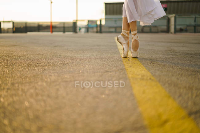 Нижняя часть балерины в точечной обуви стоит на желтой линии на городской дороге — стоковое фото
