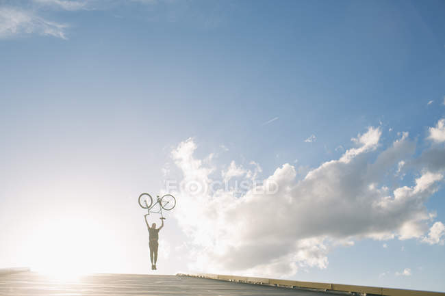 Silhueta de menino com bicicleta acima da cabeça — Fotografia de Stock