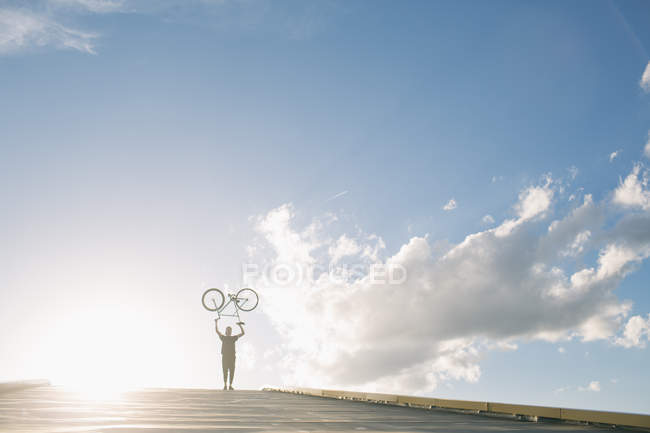 Silhouette of boy with bike above head — Stock Photo
