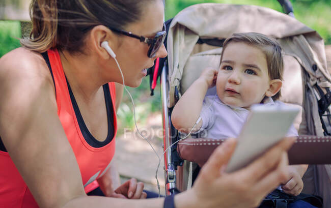 Portrait of adult woman listening to music via phone with her son in stroller — Stock Photo