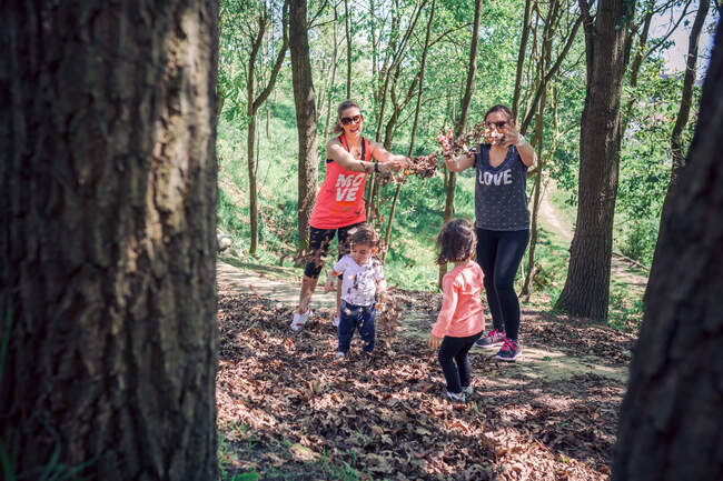 Le mamme lanciano fogliame autunnale sui bambini nella foresta — Foto stock