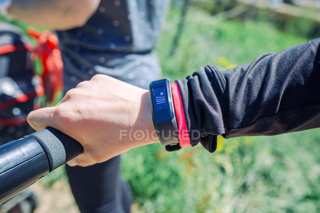 Unrecognizable female hand with fitness bracelet showing pulse while pushing pram in park in sunlight — Stock Photo