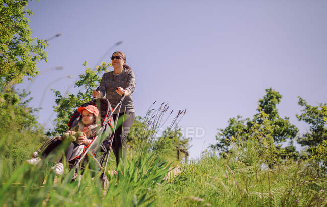 Low perspective of walking mother in park with pram.Copy space — Stock Photo