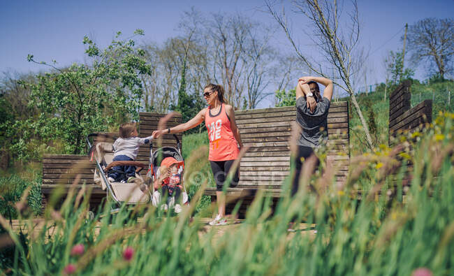 Madri adulte che si allungano nel parco soleggiato con i loro bambini in passeggini — Foto stock