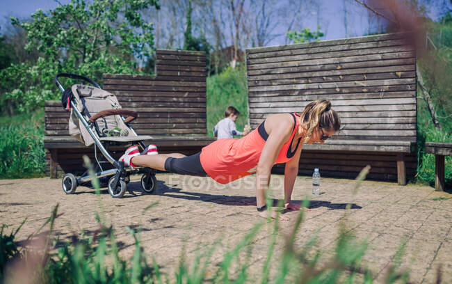 Vista lateral de mamá deportista haciendo ejercicio mientras el niño camina detrás - foto de stock