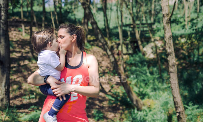 Ritratto di donna con bambino sulle braccia che lo bacia nel parco — Foto stock