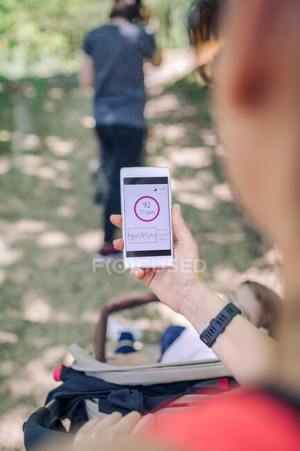 Крупним планом невизначена жінка тримає мобільний телефон, що показує пульс після фізичних вправ в парку — стокове фото