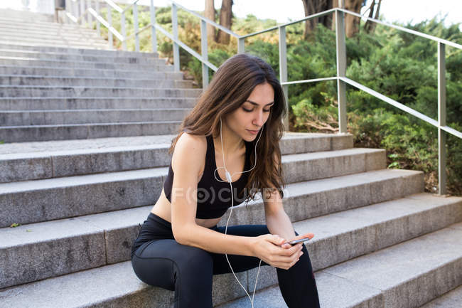 Sportliche junge Frau sitzt auf der Treppe und hört Musik. — Stockfoto