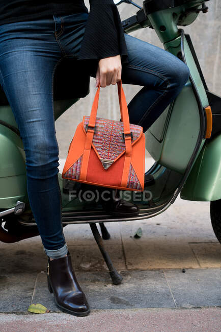 Una donna irriconoscibile che tiene una borsa arancione seduta sullo scooter. — Foto stock