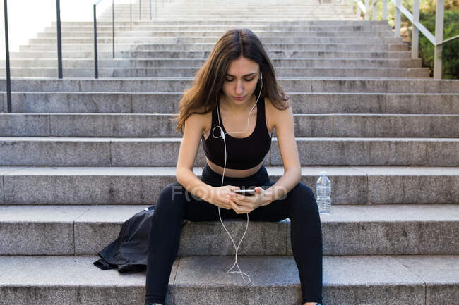 Sportive young woman on stairs taking rest and listening to music. — Stock Photo