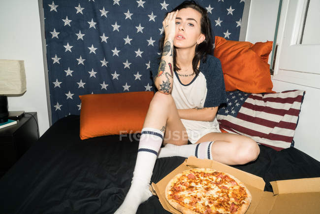 Молода жінка сидить на ліжку з піцою — стокове фото
