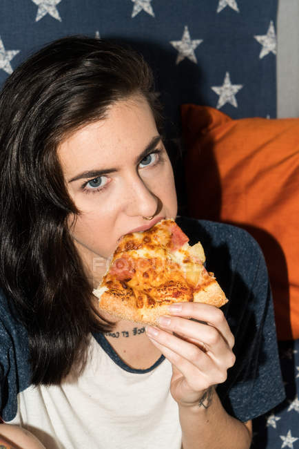 Woman eating pizza and looking at camera — Stock Photo