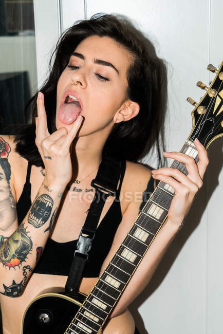 Женщина с гитарой делает рок-знак — стоковое фото