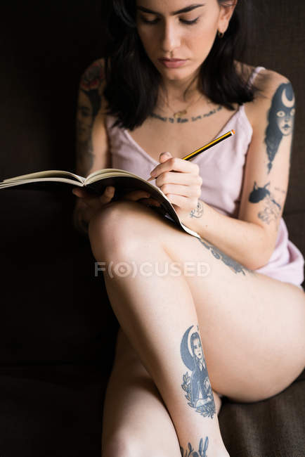 Tattooed woman writing in notebook — Stock Photo