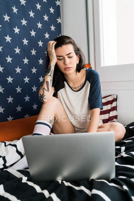 Jeune femme assise au lit avec ordinateur portable — Photo de stock