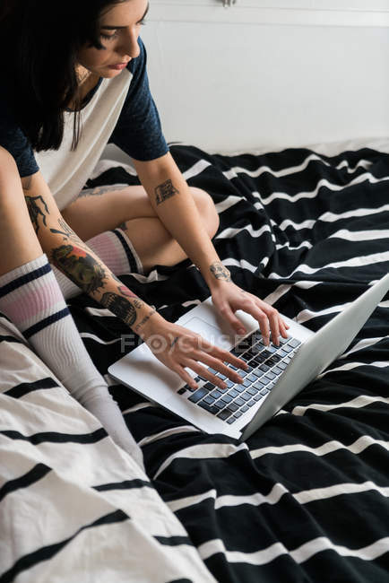 Женщина печатает на ноутбуке сидя на кровати — стоковое фото