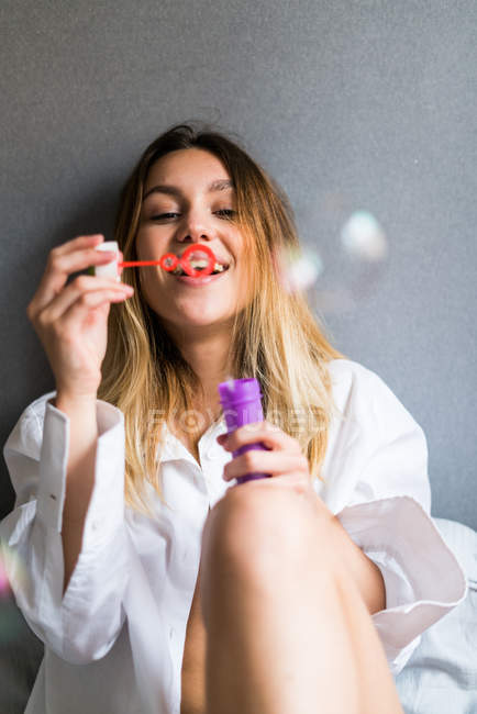 Woman blowing bubbles lying on bed — Stock Photo