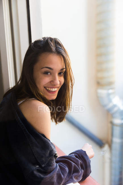 Sonriente chica fumando en ventana - foto de stock